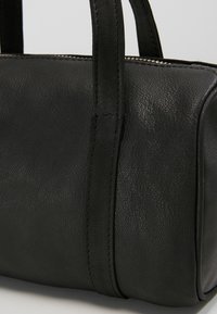 Czarna skórzana torba na ramię o gładkiej strukturze, z krótkimi uchwytami i prostokątnym kształtem, widocznymi szwami oraz zapięciem na zamek.