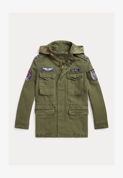 Ελαιοπράσινο στρατιωτικού στυλ μπουφάν, από βαμβακερό ύφασμα, έχει κουκούλα, δύο τσέπες στο στήθος και κεντητές ετικέτες στους ώμους. Κλείνει με φερμουάρ και κουμπιά.