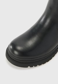 Stivale alla caviglia in pelle nera con finitura liscia, punta arrotondata e suola in gomma testurizzata. Design minimalista, senza hardware o motivi visibili.