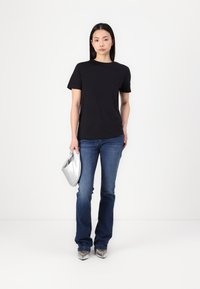 Black short-sleeve T-shirt, blue flared jeans, and silver clutch. Model wears silver high-heeled shoes. Simple design, clean lines, casual look.