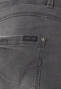 Grijze denim jeans met een zwart label met de tekst "ONLY", zilverkleurige details en subtiele stikselaccenten. Soepele textuur met een klassieke pasvorm.