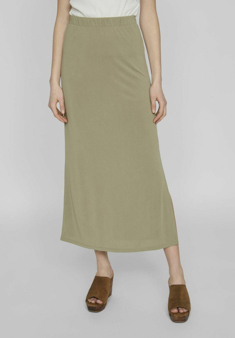 Falda larga de jersey verde oliva con una cinturilla elástica, que presenta una abertura lateral y una textura suave. Combinada con sandalias de cuña marrones.