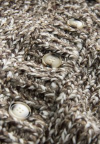 Close-up of knitted brown and white wool fabric with three beige four-hole buttons sewn on.