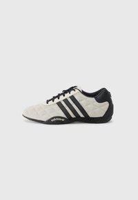 Adidas športna obutev s teksturiranim svetlo sivim zgornjim delom in črnimi usnjenimi detajli. Ima črn logo s tremi črtami in oblazinjeno podplatom.