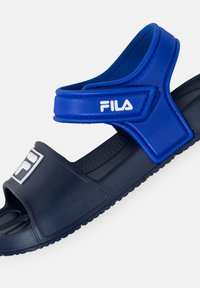 Sininen ja tummansininen liukuva sandaali säädettävällä hihnalla, tekstuuripohjalla ja logoyksityiskohdalla. Valmistettu synteettisestä materiaalista; helposti päälle puettava malli.