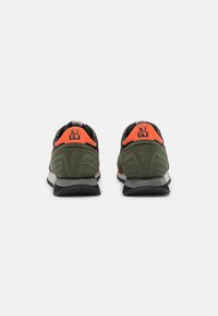 Zapatillas deportivas de color verde oliva con detalles en negro y una lengüeta en el talón de color naranja brillante. Cuentan con una suela acolchada y parte superior de tela texturizada.