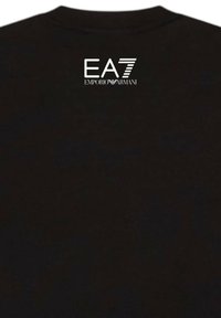 T-shirt nera con collo rotondo. Presenta un logo bianco EA7 Emporio Armani sulla parte superiore della schiena. Il tessuto appare liscio e leggero.