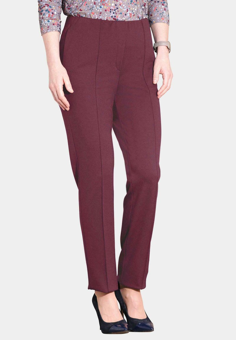 Bordeaux geklede broek met een nauwsluitende pasvorm, soepel materiaal, plooien aan de voorkant en zijzakken, gecombineerd met marineblauwe hakken en een bedrukte top.