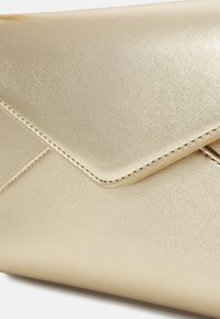 Pochette enveloppe dorée avec une finition métallique lisse, dotée d'un rabat pointu et de coutures subtiles le long des bords.