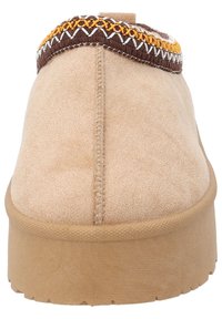 Beige ruskinds hjemmefutter med brun og gul dekorativ syning langs toppen. Flad sål med struktureret gummi for greb. Glat overflade.