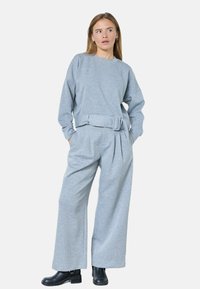 Sudadera gris con mangas anchas y cintura ceñida con cinturón, combinada con pantalones plisados grises. Botines negros completan el conjunto.