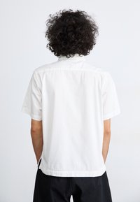 Short-sleeve, white, cotton shirt with a relaxed fit, featuring a button-down collar and side slits at the hem.