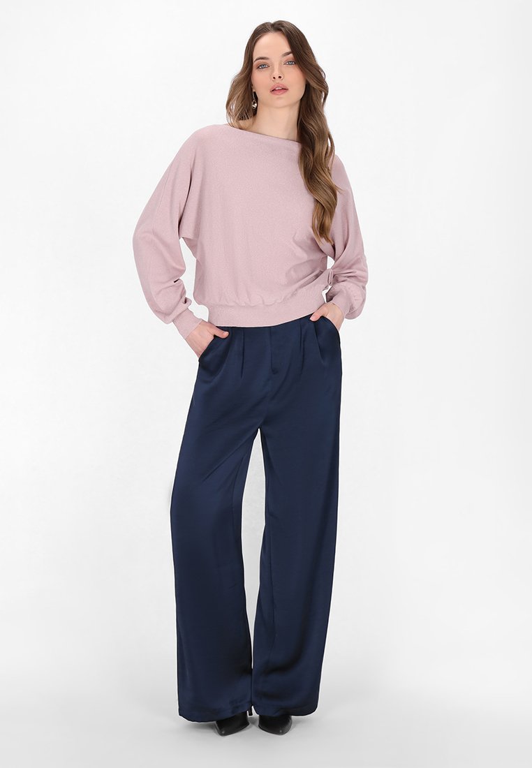 Lichtroze oversized trui met geribde zoom, gecombineerd met donkerblauwe wijde broek. Glad textiel en een relaxte pasvorm.