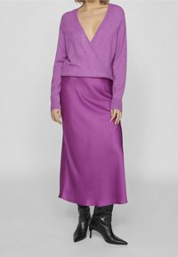 Fialový pletený svetr s výstřihem do V ve spojení s dlouhou saténovou sukni v barvě magenta. Outfit doplňují černé kotníkové boty na vysokém podpatku.