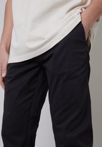 Camicia bianca strutturata con orlo sovrapposto a pantaloni neri con tasche laterali, realizzati in tessuto liscio e con un design a gamba dritta.