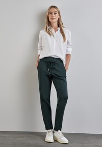Vit långärmad skjorta med knappar i kombination med mörkgröna slim fit-byxor som har dragsko i midjan och silverdetaljer. Bärs med vita sneakers.