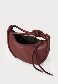 Bolso de piel burdeos con una correa anudada, cierre con cremallera, textura suave y bolsillo interior, con un diseño minimalista.