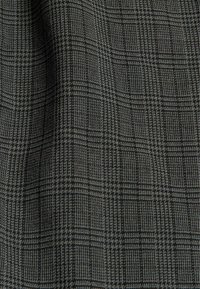 Tissu noir et gris avec un motif pied-de-poule et à carreaux texturé, montrant des plis suggérant un matériau doux et tissé.