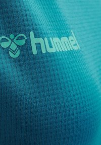 Vêtements de sport bleu sarcelle avec une texture côtelée. Présente un logo discret dans une teinte plus claire. Le matériau semble extensible et respirant.