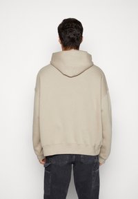 Beige oversized hoodie met een grote capuchon, verlaagde schouders en een geribde zoom, gecombineerd met donkere jeans met een cargozak.