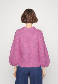Pull rose tricoté épais avec un col rond, des manches bouffantes et une finition texturée, associé à un pantalon en jean à jambes larges.
