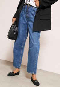Modré džínové kalhoty s vysokým pasem a volným střihem, klasický design s pěti kapsami, doplněné černými mokasínami a černým sakem.