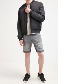 Chaqueta bombers negra, camiseta gris, pantalones cortos de mezclilla gris desgastados y zapatillas deportivas negras. Diseño sencillo con puños doblados y costuras visibles.