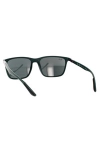 Occhiali da sole in plastica verde con lenti grigio scuro, forma quadrata e aste sottili con un accento marrone. Le lenti offrono protezione UV.