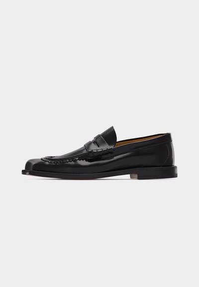 Μαύρο δερμάτινο μοκασίνι τύπου penny loafer με λείο, γυαλιστερό φινίρισμα και χαμηλό συσσωρευμένο τακούνι, απεικονιζόμενο σε προφίλ σε απλό φόντο.