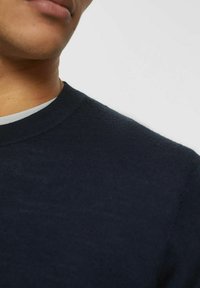 Maglione lavorato a maglia di colore blu navy con scollatura a girocollo, caratterizzato da una superficie liscia e un design aderente. Vista ravvicinata del colletto e dell'area delle spalle.
