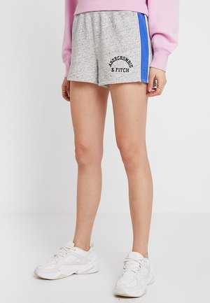 Modelo vistiendo pantalones cortos deportivos grises con franjas laterales azules y texto "Abercrombie & Fitch", zapatillas blancas y una sudadera rosa.