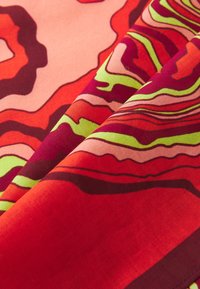 Red and pink patterned fabric featuring wavy lines in shades of green, maroon, and light pink; smooth texture with a soft drape.