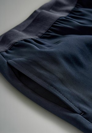 Marineblå stofshorts med en plisseret talje og glat tekstur. Har stikninger og et minimalistisk design.