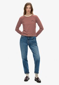 Langarmige rood en crèmekleurige gestreepte shirt met een ronde hals, gecombineerd met losse blauwe denim jeans en donkere loafers, staande op een lichte achtergrond.