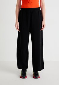 Black wide-leg pants with an elastic waistband, made of soft fabric, paired with stylish footwear featuring bright accents and a textured design.
