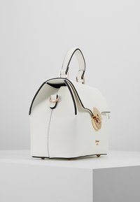 Valkoinen nahkalaukku, jossa on jämäkkä muoto, mustat yksityiskohdat, kultainen pyöreä solki ja lyhyet kahvat, joissa on tekstuuripinta.