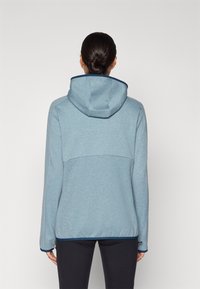 Moleton azul claro feito de fleece macio, com capuz ajustável, acabamento escuro e um design ajustado com mangas longas e corte até à cintura.