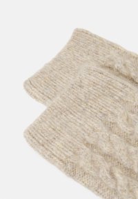 Beige adīta šalle, kas izgatavota no mīksta vilnas maisījuma, ar faktūru ribotu rakstu un ruļļveida malām. Audums izskatās silts un ērts.