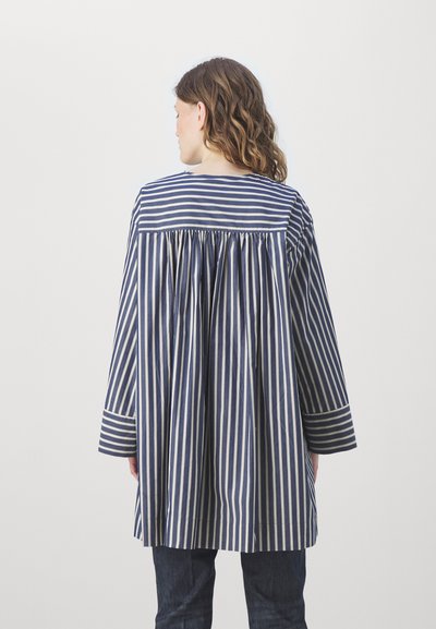 Tunique rayée en marine et crème, manches longues avec boutons de poignet, coupe ample, design au dos plissé, tissu en coton avec une texture lisse.