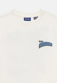 Cremefarvet bomulds T-shirt med rund halsudskæring, der har et blåt grafisk tryk med teksten "Hilsener fra COLORADO" på brystet.