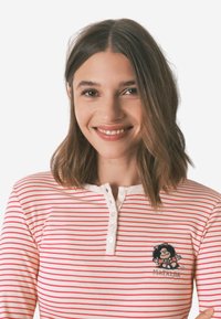 Hvid- og rødstribet langærmet skjorte med henley-udskæring, der har en flerfarvet broderet tegnefilmsfigur på venstre bryst.