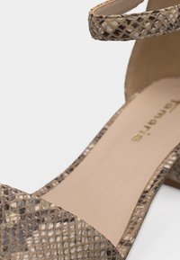 Sandale à bout ouvert avec motif python beige et marron, bride à la cheville et semelle intérieure beige rembourrée avec nom de la marque visible.