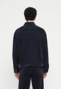 Σκούρο μπλε τζάκετ από κοτλέ ύφασμα με κλασικό γιακά, φαρδιά γραμμή και κουμπιά στα μανίκια. Διακρίνονται ραφές στη πλάτη.