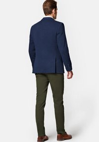 Granatowa marynarka o fakturze z klapami typu notch, z jednym rozcięciem, w zestawie z oliwkowymi spodniami i brązowym obuwiem, widok z tyłu.