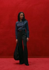 Camicia azzurra a maniche lunghe con bottoni, pantaloni neri a vita alta e svasati, cintura nera e borsa a tracolla nera. Tessuto morbido, elementi di design minimali.