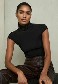 Must mustrikkidega must turtleneck, millele sobivad kitsad pruunid nahkpüksid. Sile kangas ja puhas, minimalistlik disain.