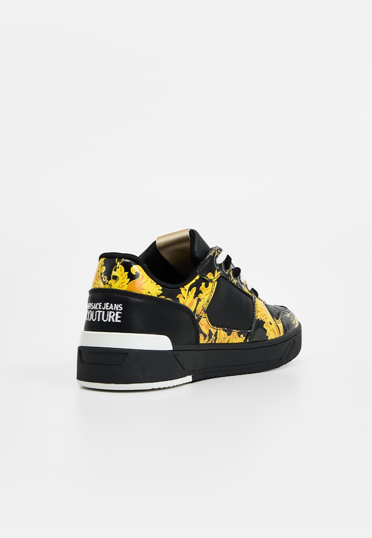 Baskets à motifs noir et jaune avec lacets, marquées "Versace Jeans Couture" sur le talon, positionnées sur un fond blanc uni.