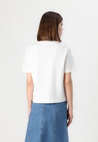 T-shirt blanc en coton avec des manches courtes et un col rond, associé à une jupe en denim bleue. Texture lisse, design simple.