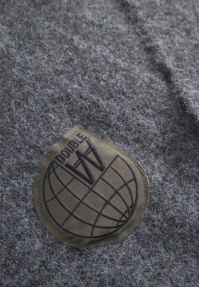 Grijze viltstof met een gestructureerde patch met een wereldbolontwerp en de tekst "DOUBLE W" in donkerbruin, gestikt langs de rand.
