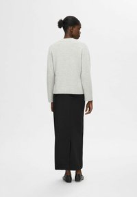 Šviesiai pilkas megztinis su ilgomis rankovėmis ir įsiūtu apvadu, derinamas su juoda, kulkšnių ilgio sijonu su užpakaliniu skeltuku, avalynė nematoma.